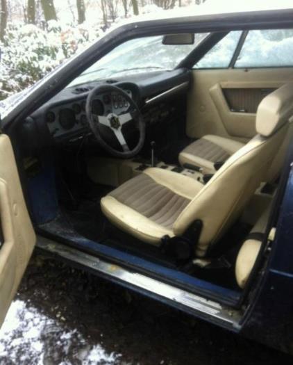 The GT4’s left-hand-drive cabin before restoration, showing beige seats with fabric inserts, beige door trim, a black dashboard and a three-spoke steering wheel.