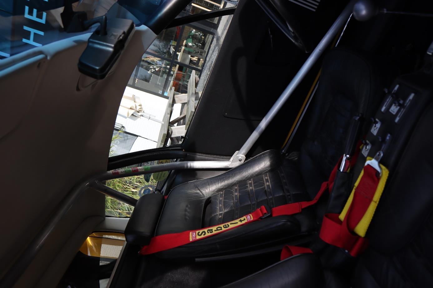 Modified Boxer cabin with a black bucket seat, red harness, metal gearshift console and roll-cage tubing.