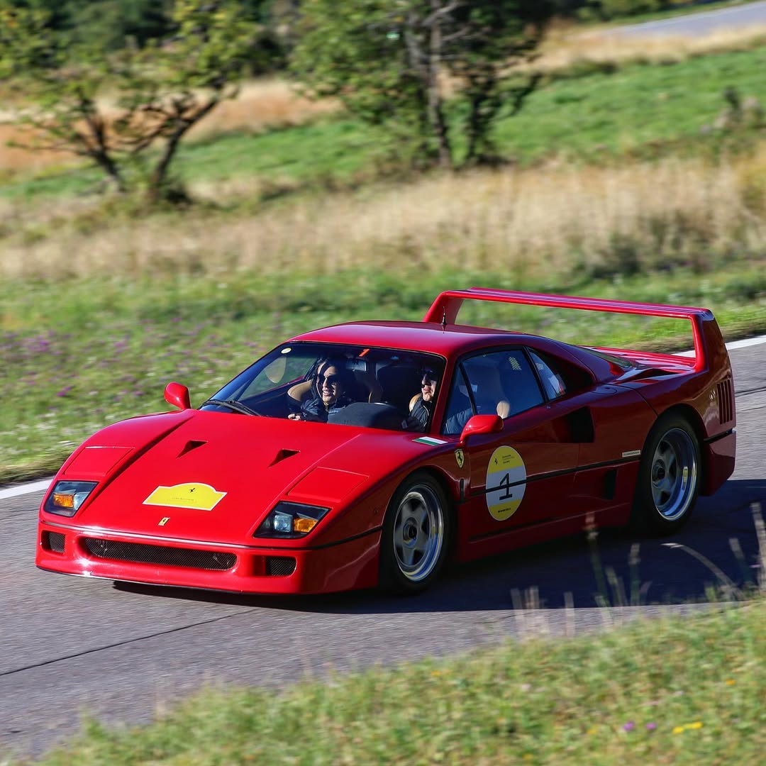 Red Ferrari F40 driving along a road with event number 4, beige-looking seats and a small roof antenna.